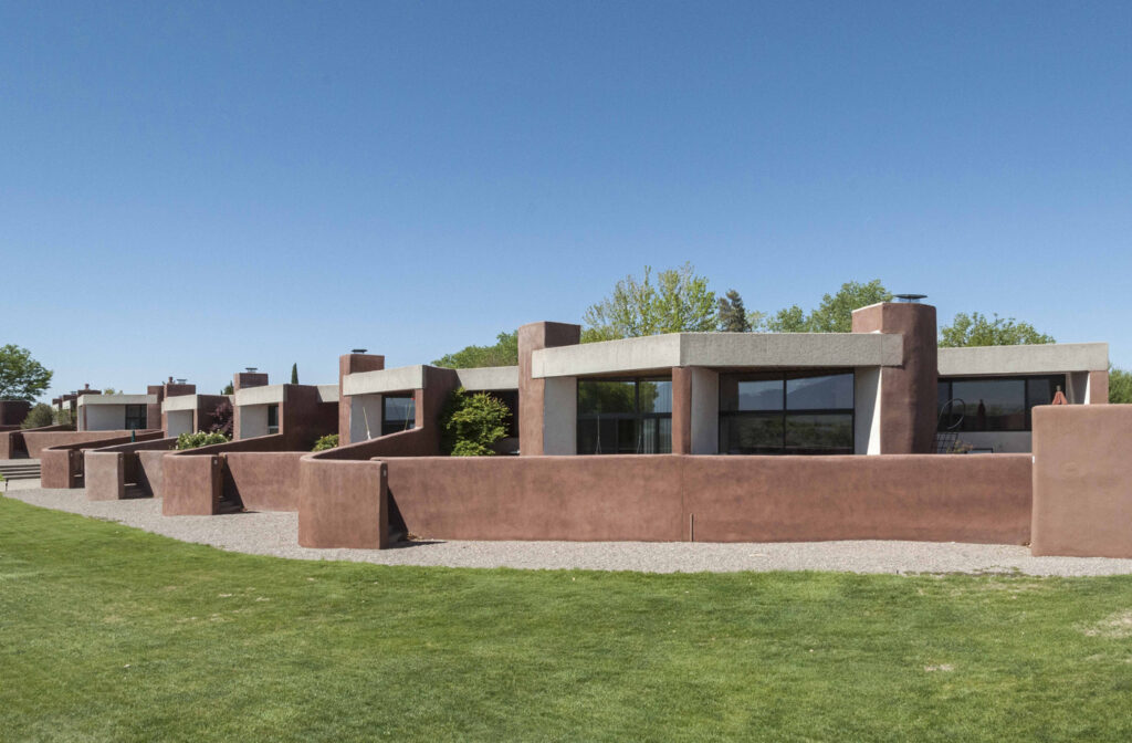 modern adobe fence in front of glass and geometric rooftop bifurcated with cylindrical column against a blue cloudy sky