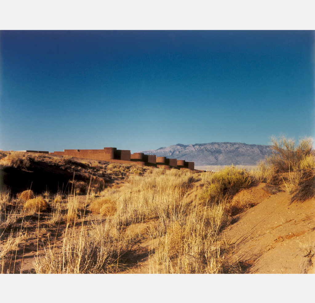 distant view of adobe townhouses in front of mountains and surrounded by desert grasses